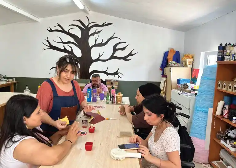 Atölye masası etrafında katılımcılar deri ve kâğıtla el sanatı çalışıyor.